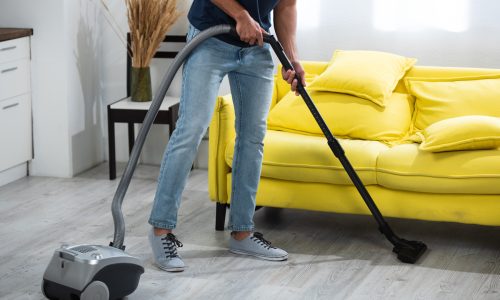 Cropped view of man cleaning floor with vacuum cleaner at home